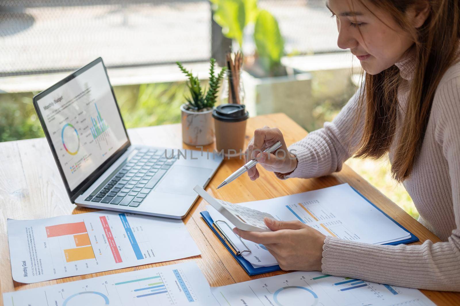 Asian woman using calculator for analysis maketing plan, Accountant calculate financial report, computer with graph chart. Business, Finance and Accounting concept
