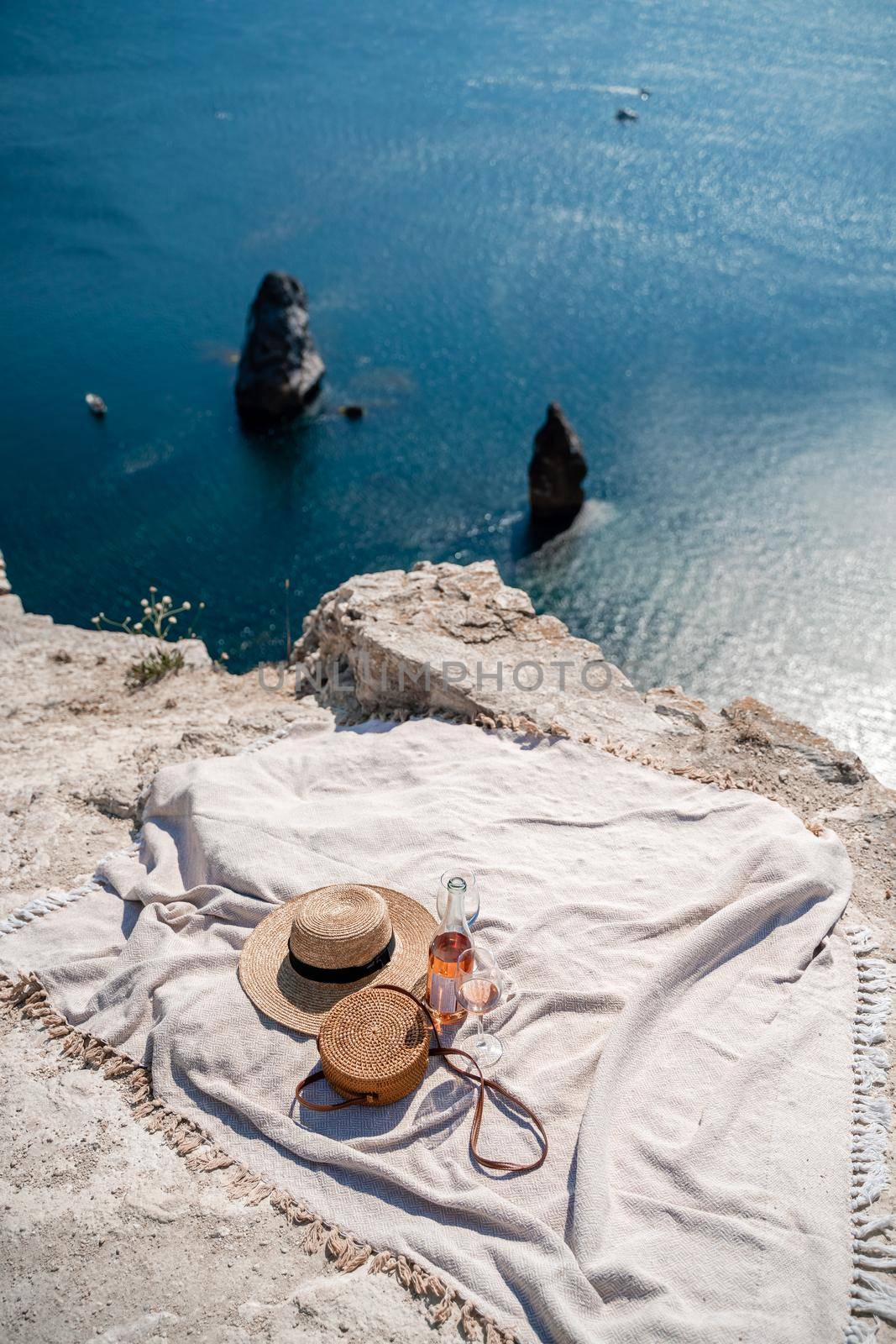 A picnic blanket, champagne, two glasses, a hat and a straw purse. Top on the mountain against the background of the sea and rocks in the sea