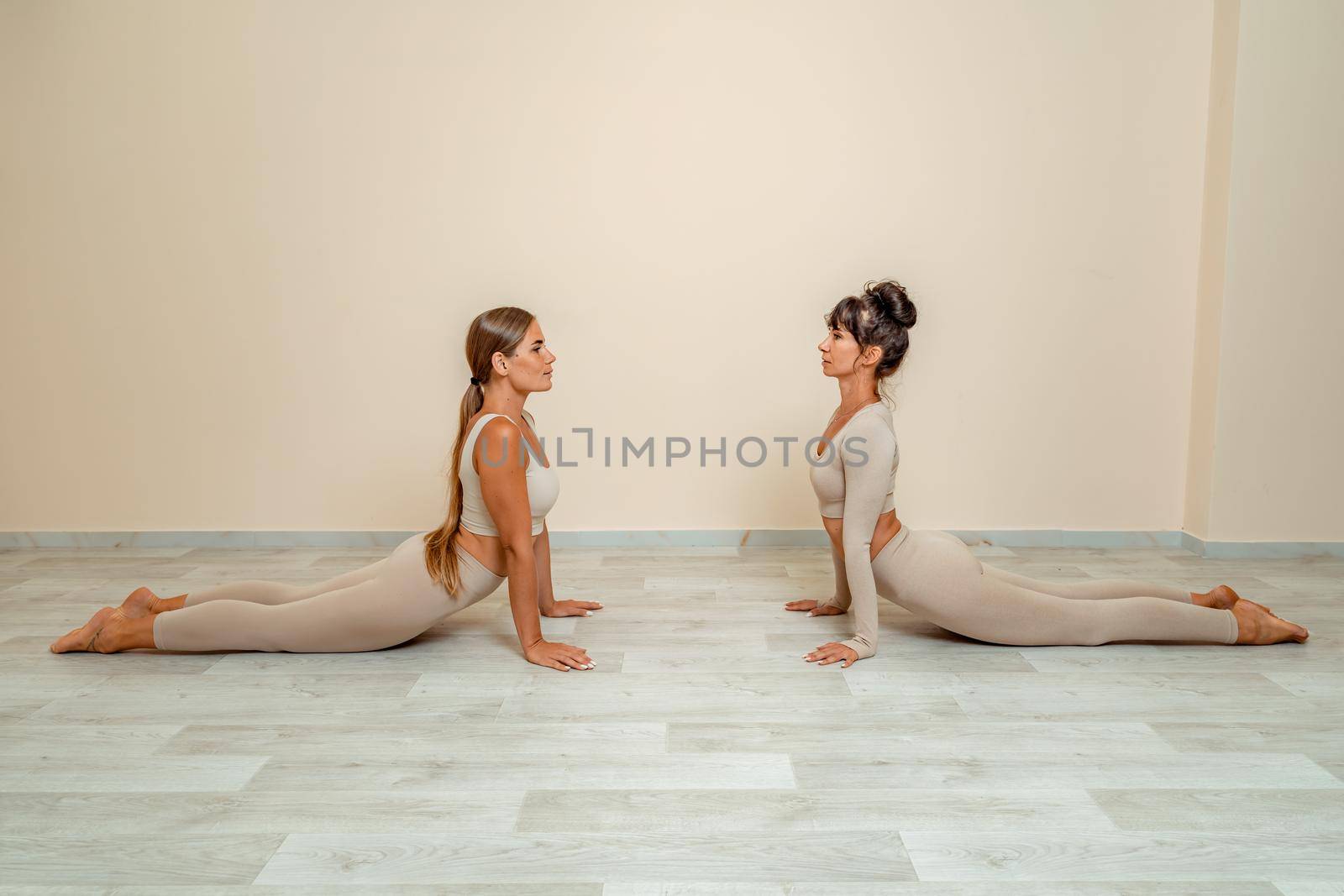 Fitness, pilates stretching exercises, a group of two attractive smiling mature women in beige sports clothes, train in a sports club. by Matiunina