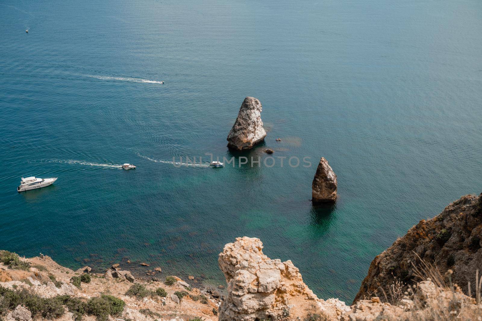 Two rocks stick out of the water in the middle of the turquoise sea. Scenic ocean view. Speed boat sails on the sea. High quality photo. by Matiunina