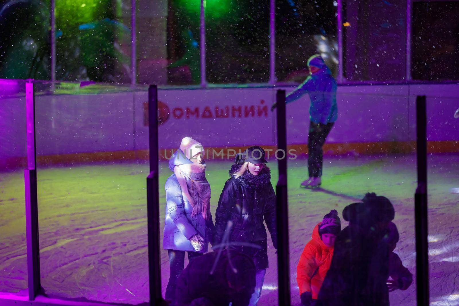 People skate in the evening on a lighted ice rink. A blizzard is raging and snow is falling. Zelenograd, Russia 28.01.2022 by Yurich32