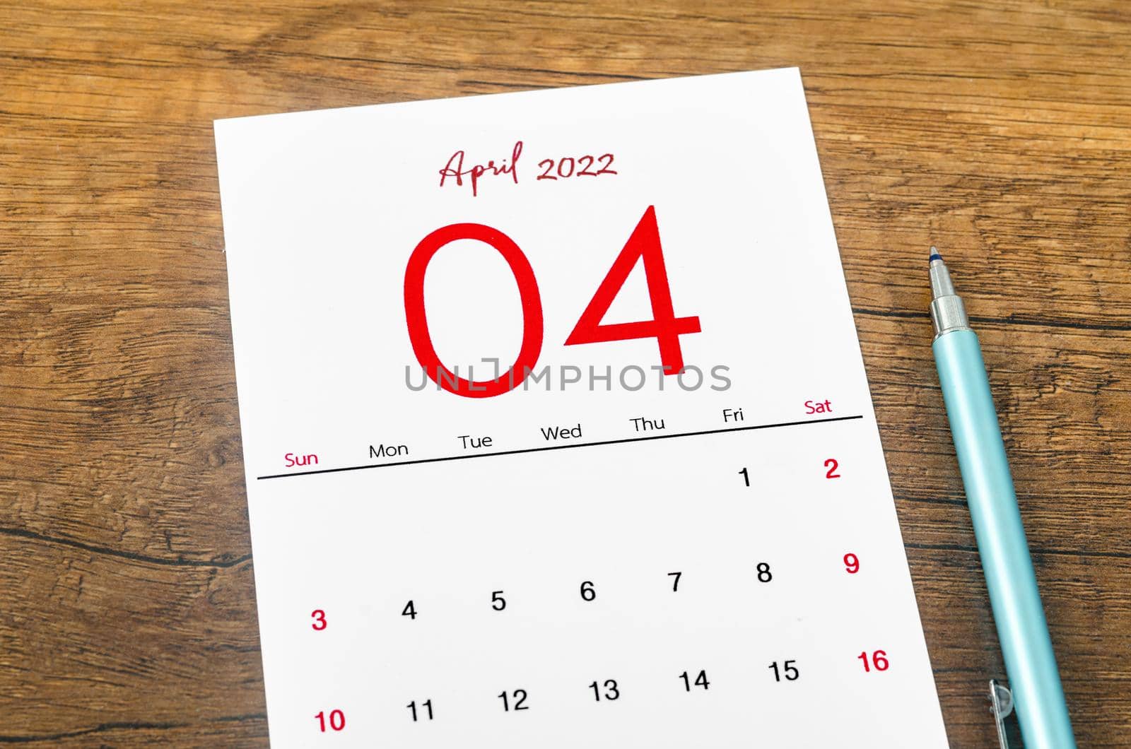 The April 2022 calendar with pen on wooden table.