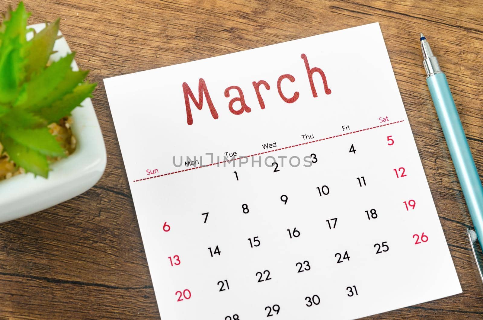 The March 2022 calendar and pen on wooden background.