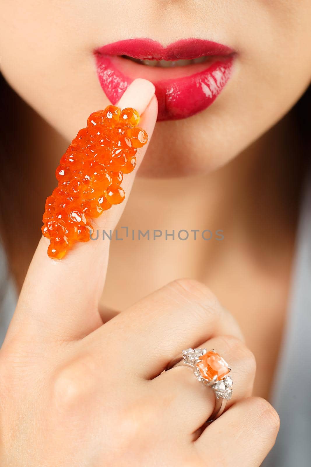 Close-up girl with red caviar on her finger. by Gravika