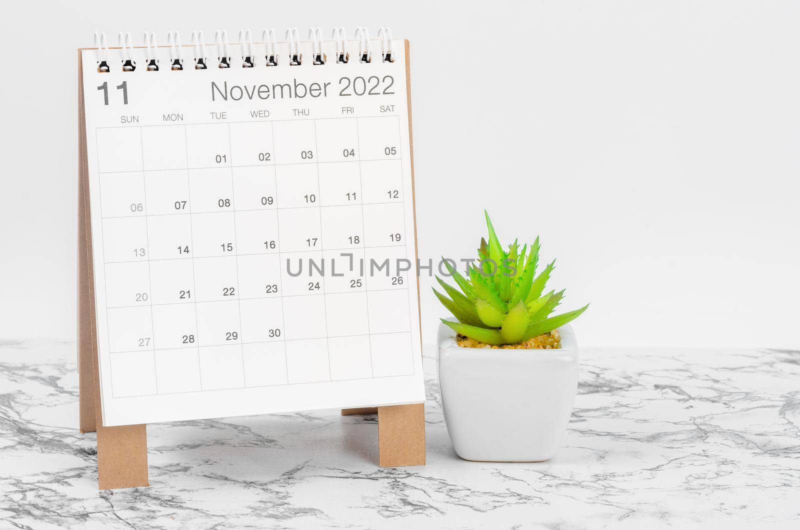 The November 2022 desk calendar with plant on marble table.