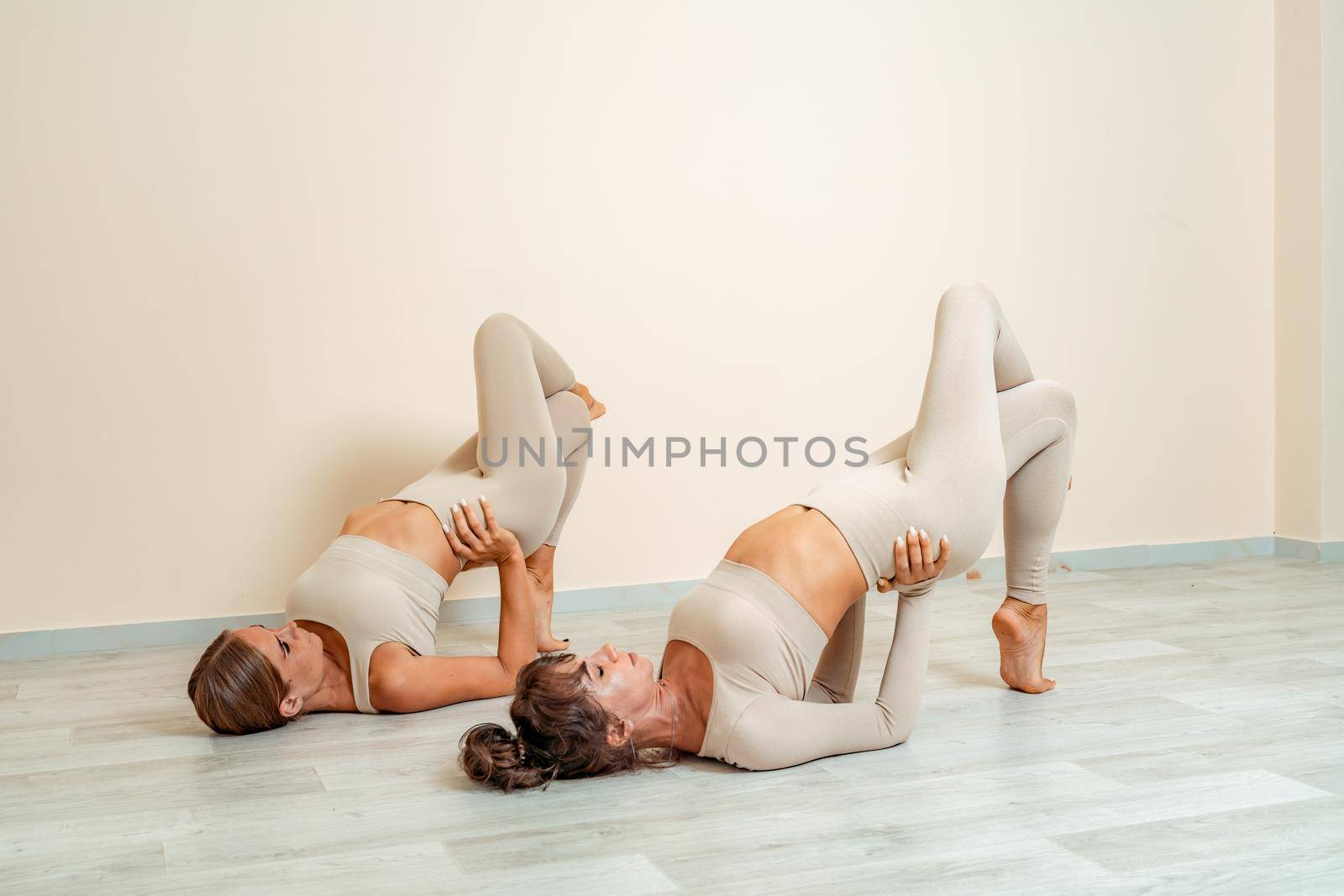 Fitness, pilates stretching exercises, a group of two attractive smiling mature women in beige sports clothes, train in a sports club. by Matiunina