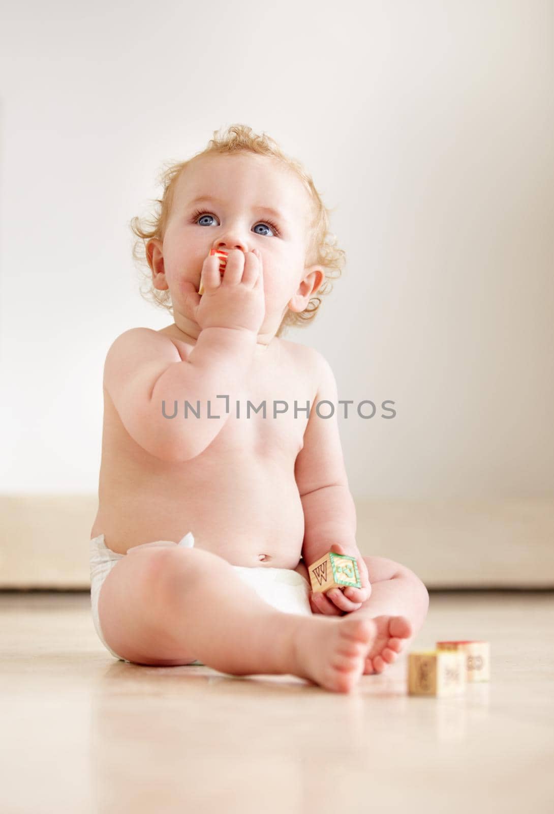 Cute baby boy looking up curiously while sitting on the floor.
