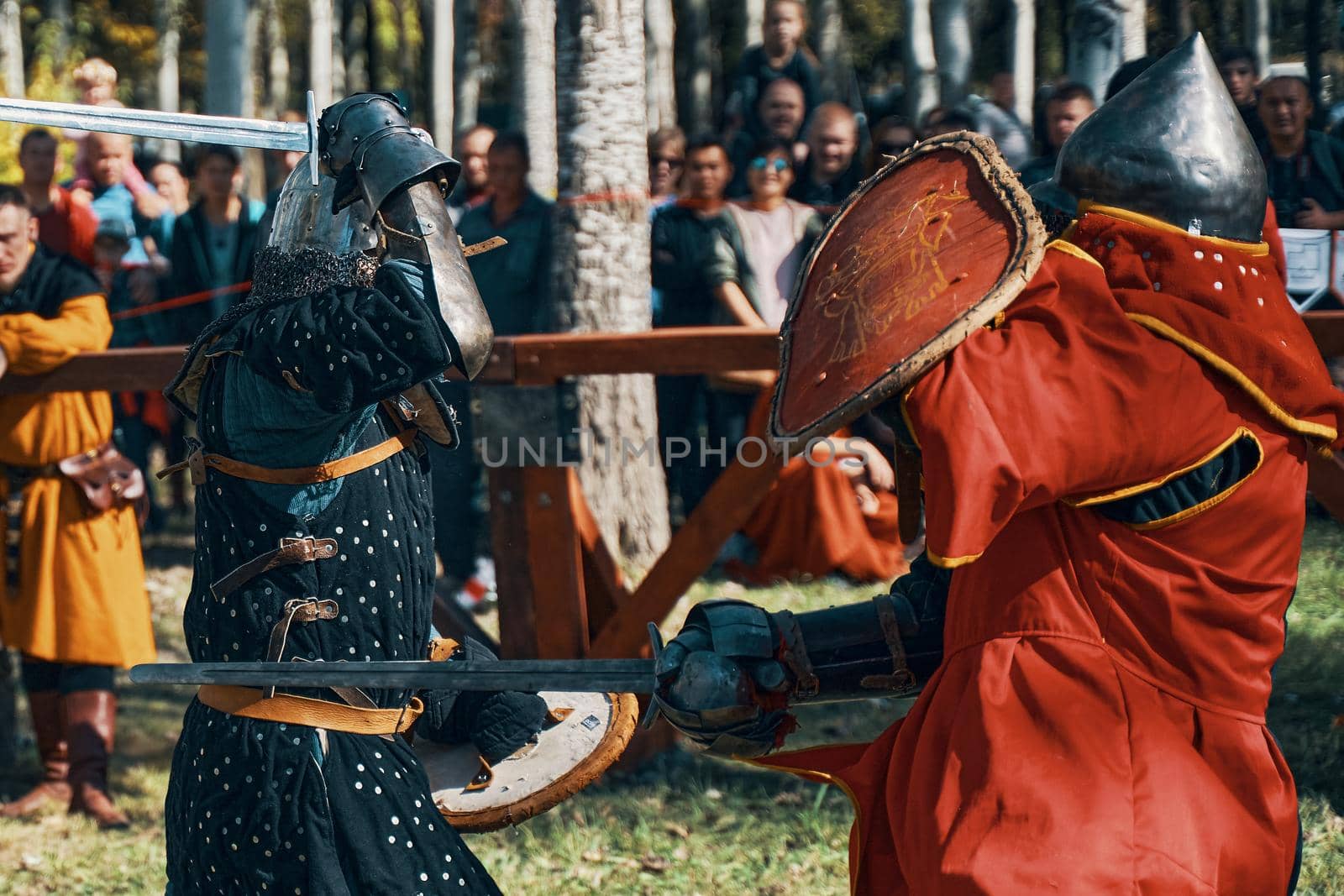 A knight in black armor against a knight in red armor in the arena. Sword fighting. Festival of historical clubs. Reconstruction of medieval battles. Bishkek, Kyrgyzstan - October 13, 2019