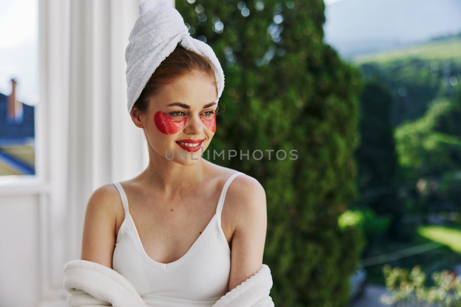Attractive young woman with a towel on his head patches on his face stands on the balcony unaltered by SHOTPRIME
