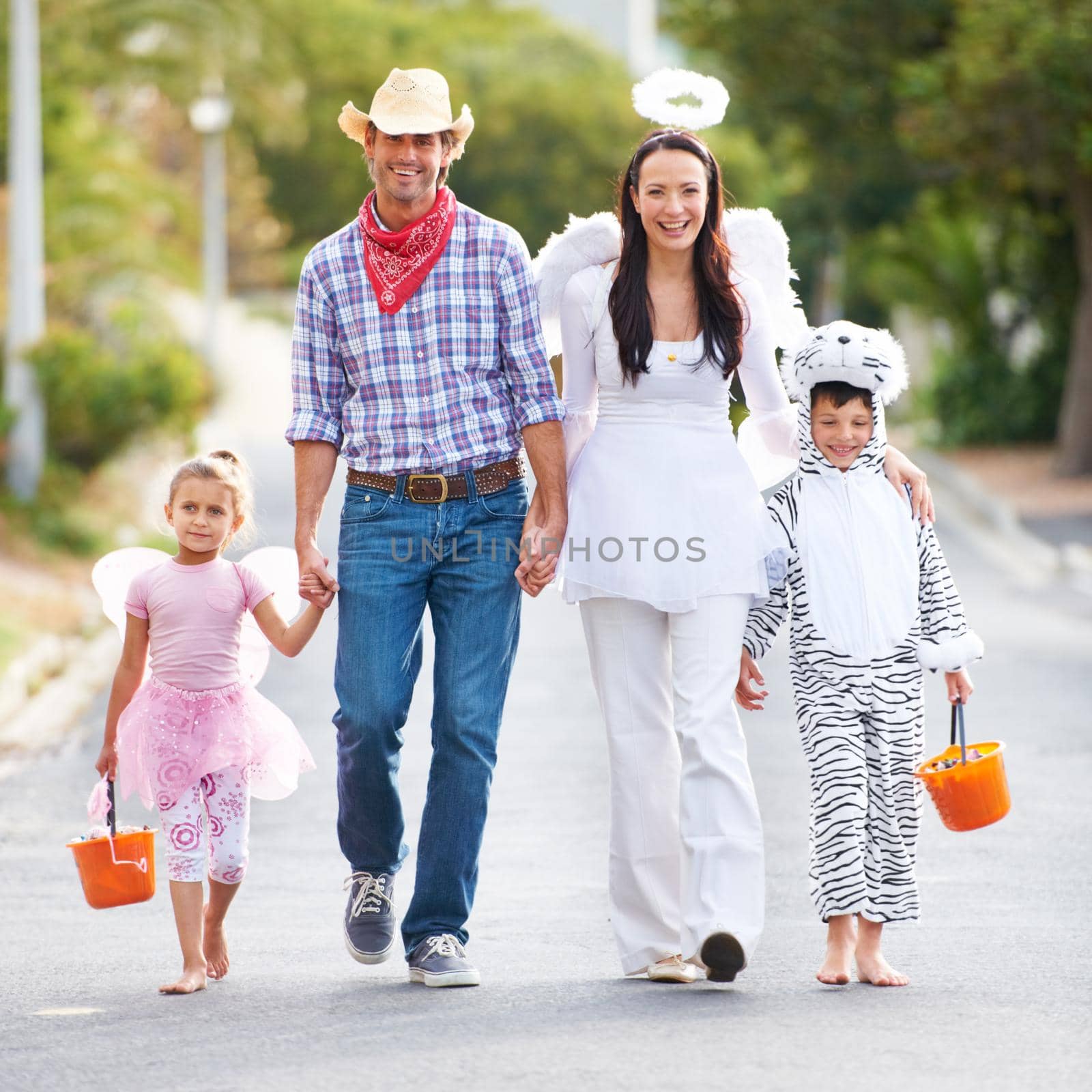 You cant beat this collection of outfits. Full length shot of a family walking down the road in their Halloween costumes. by YuriArcurs