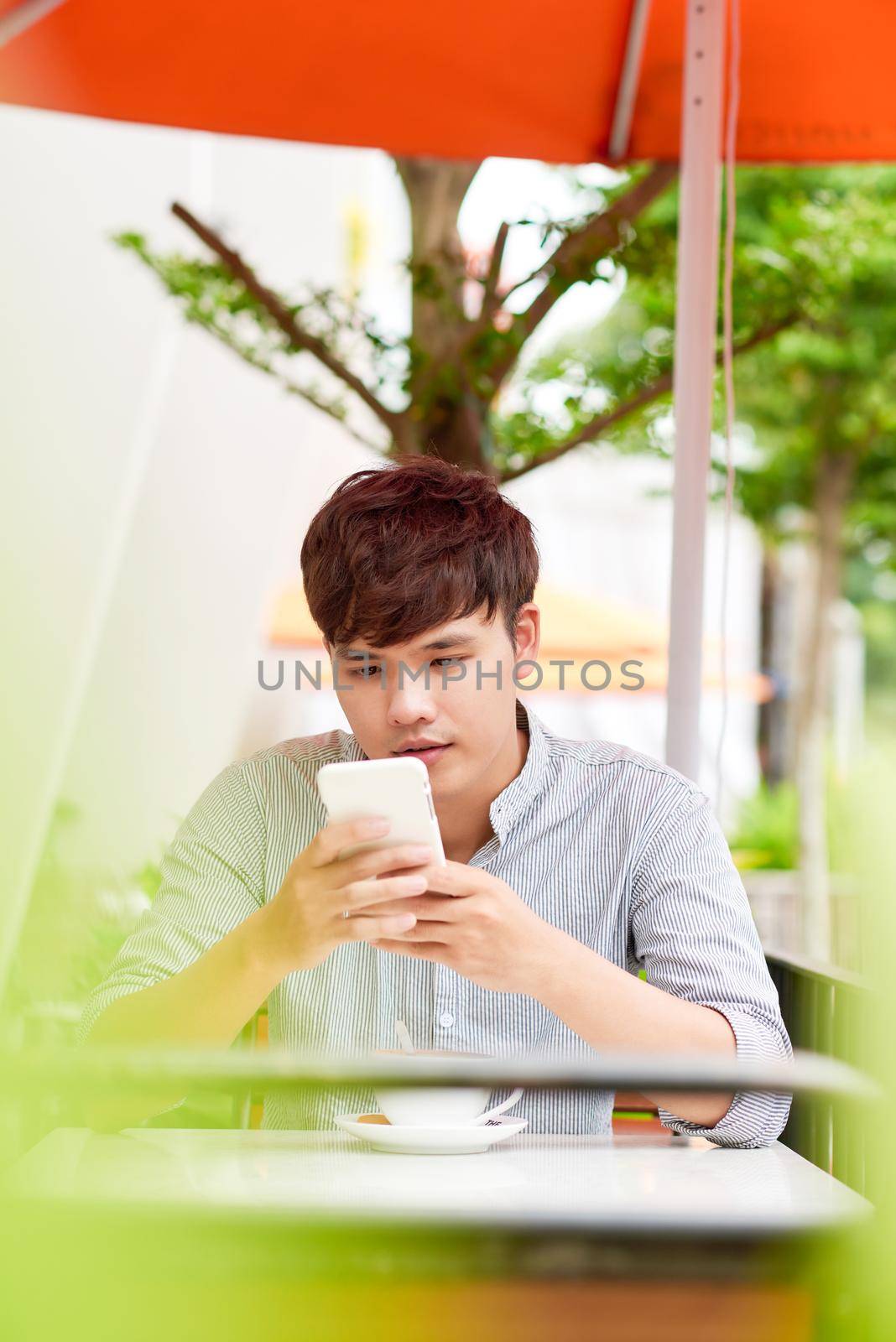 Young man in coffee shop talking on the phone. Outdoors by makidotvn