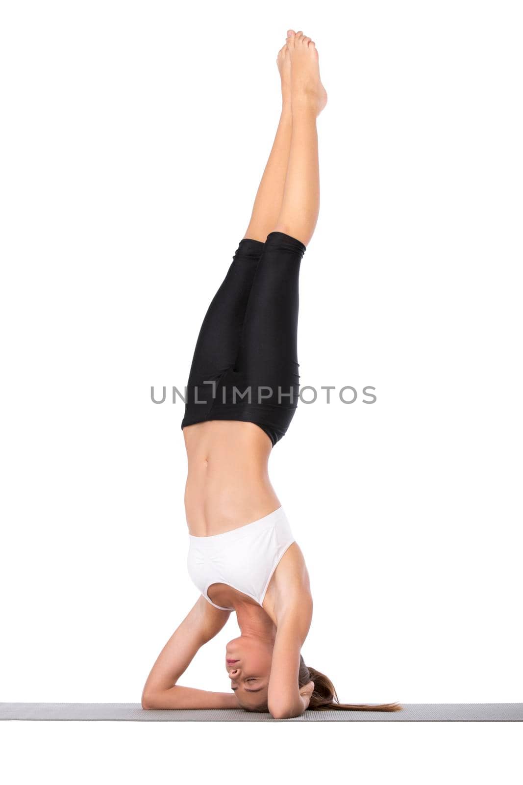 An attractive young woman standing on her head against a white background.