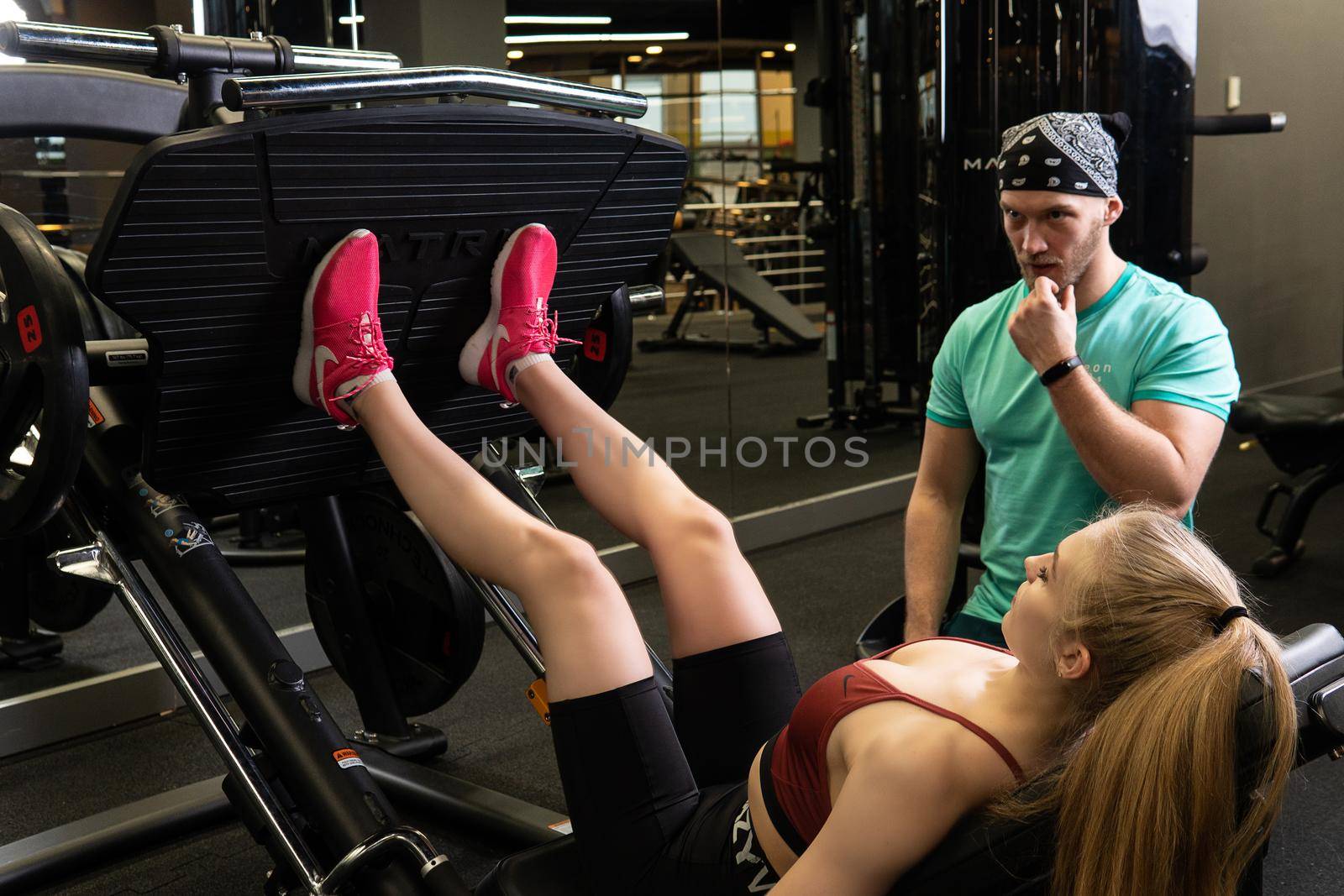 RUSSIA, MOSCOW - FEB 11, 2022: A girl is engaged in a led press simulator in a red blonde beautiful on a black background leg gym training press legs, for lifestyle strength from muscle from sport club, white male. Shape slim beautiful, adult trainer