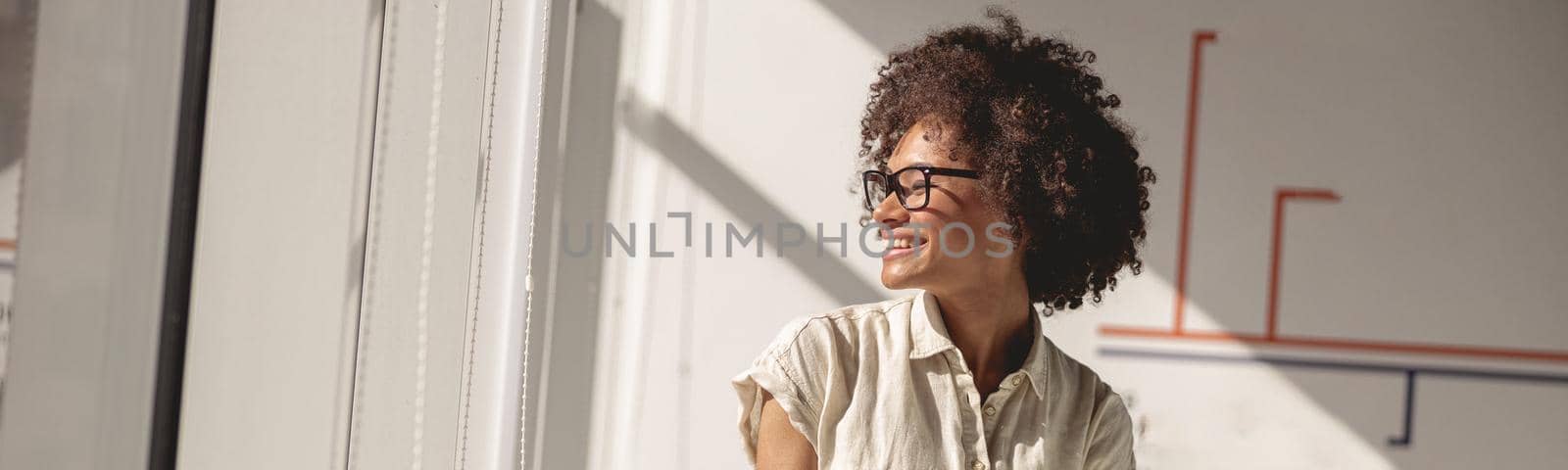 Happy Afro American female worker sitting on the table while holding notebook and looking out the window