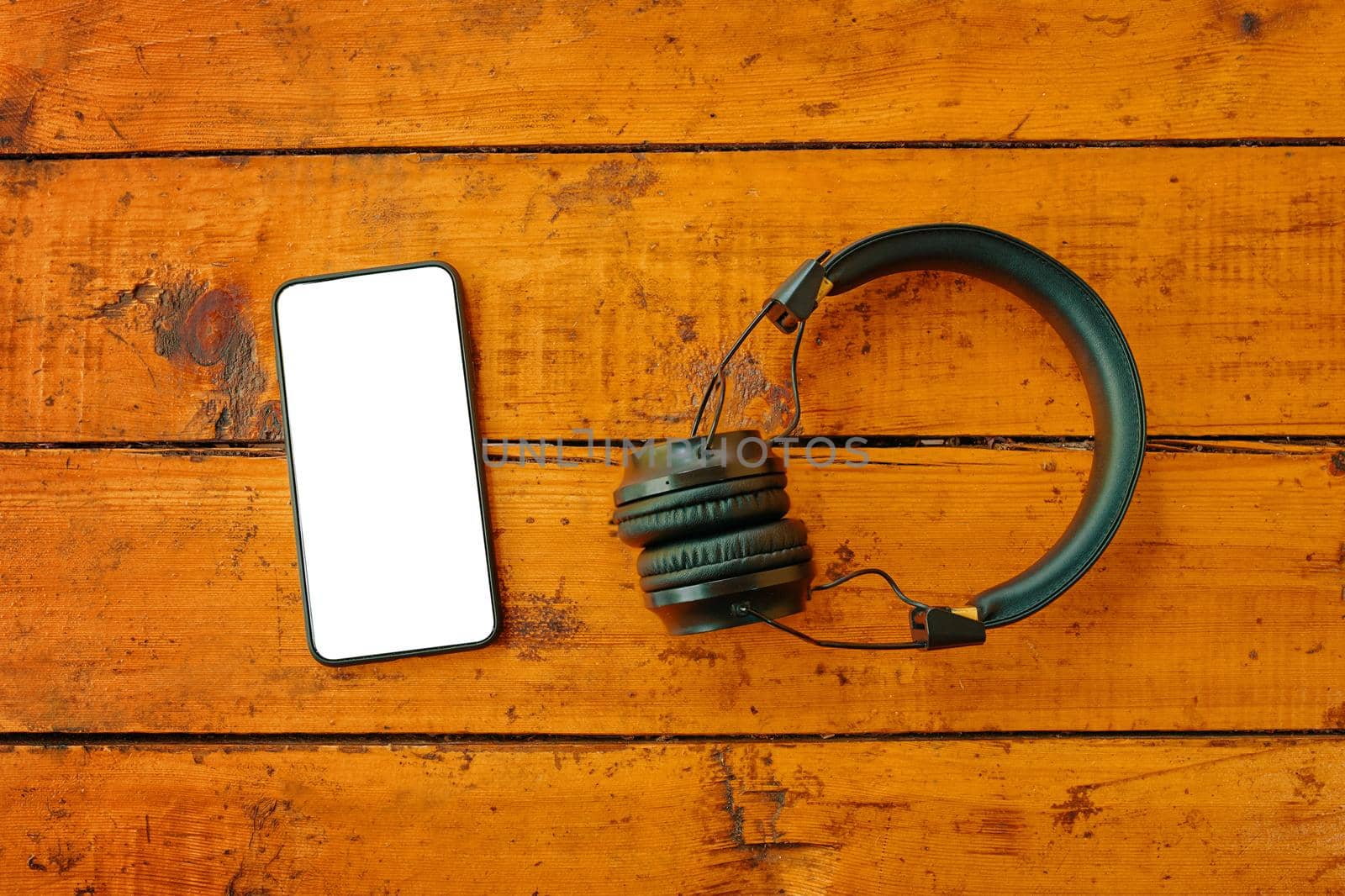 Headphones and smartphone on wooden table. Top view on mobile phone with empty screen. Instagram blogging. Copy space for text.