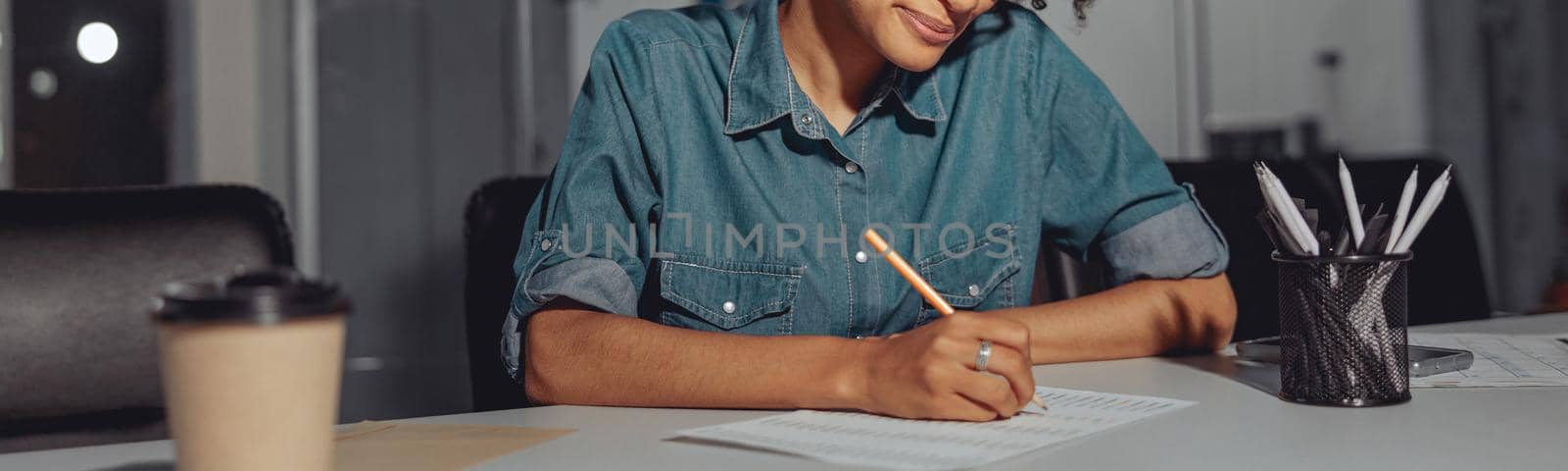 Happy Afro American lady sitting at the desk and writing on document while working in modern office