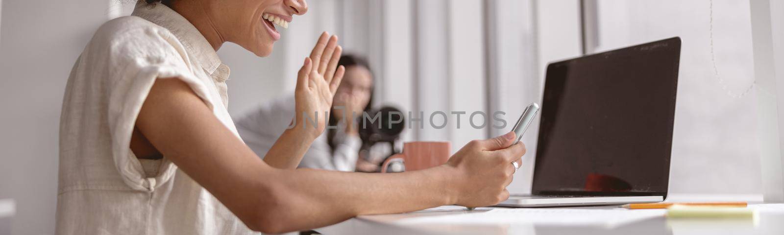 Smiling pretty multiethnic lady waving hand while making a video call on a mobile phone in the office