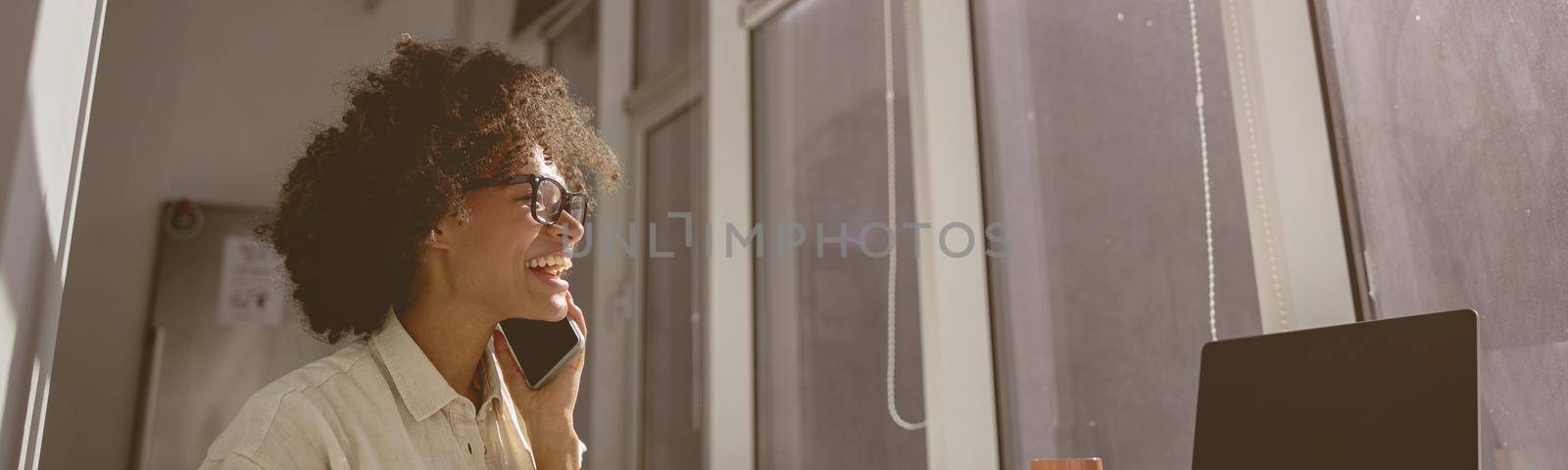 Smiling young female worker sitting at workplace in coworking while using smartphone