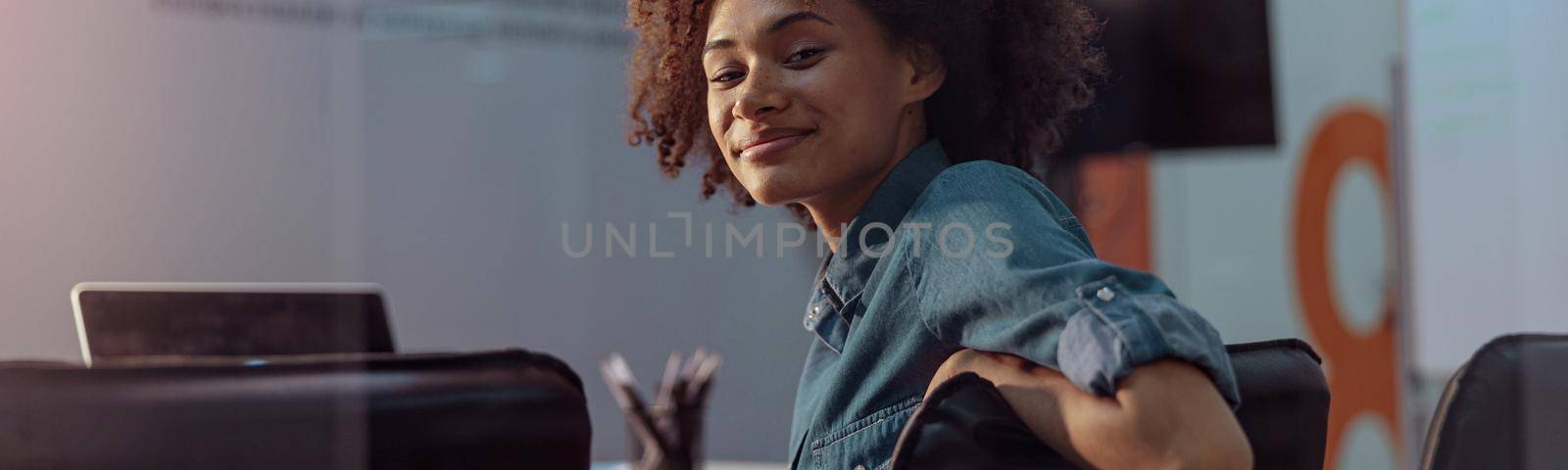 Smiling African American woman sitting on the chair in the meeting room and looking at camera