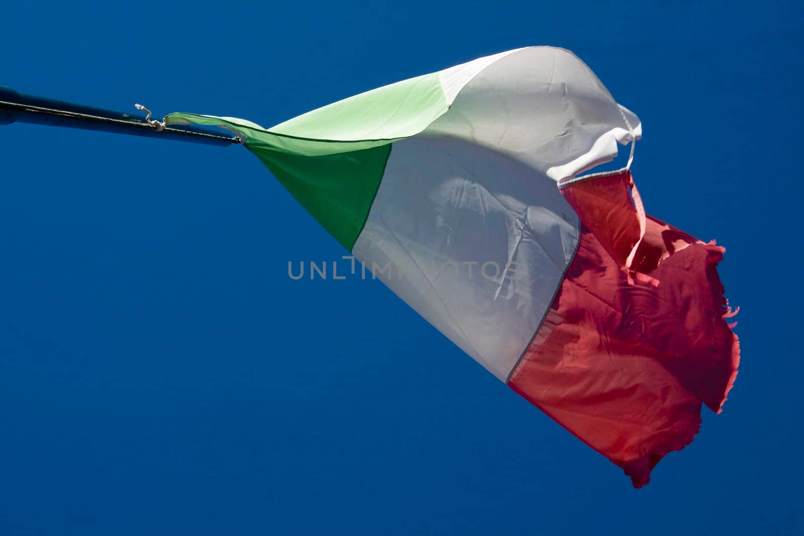 The Italian tricolor flag worn and torn by the wind in a blue sky 