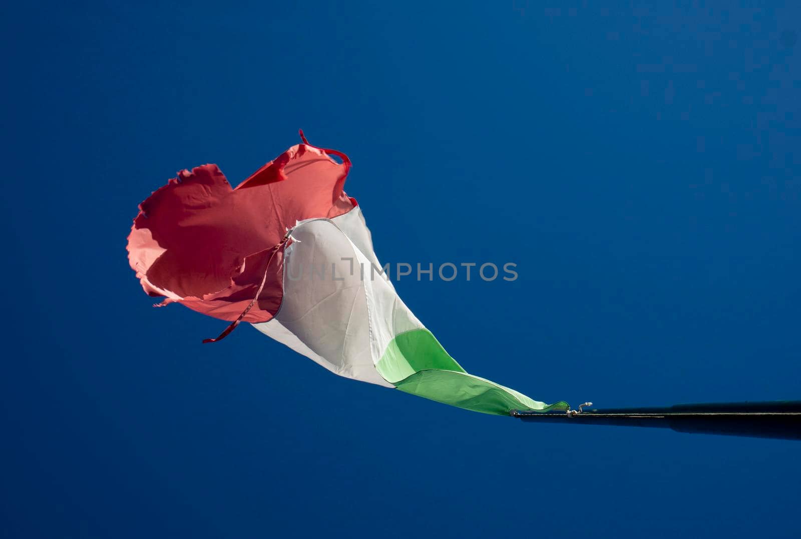 The Italian tricolor flag worn and torn by the wind in a blue sky 