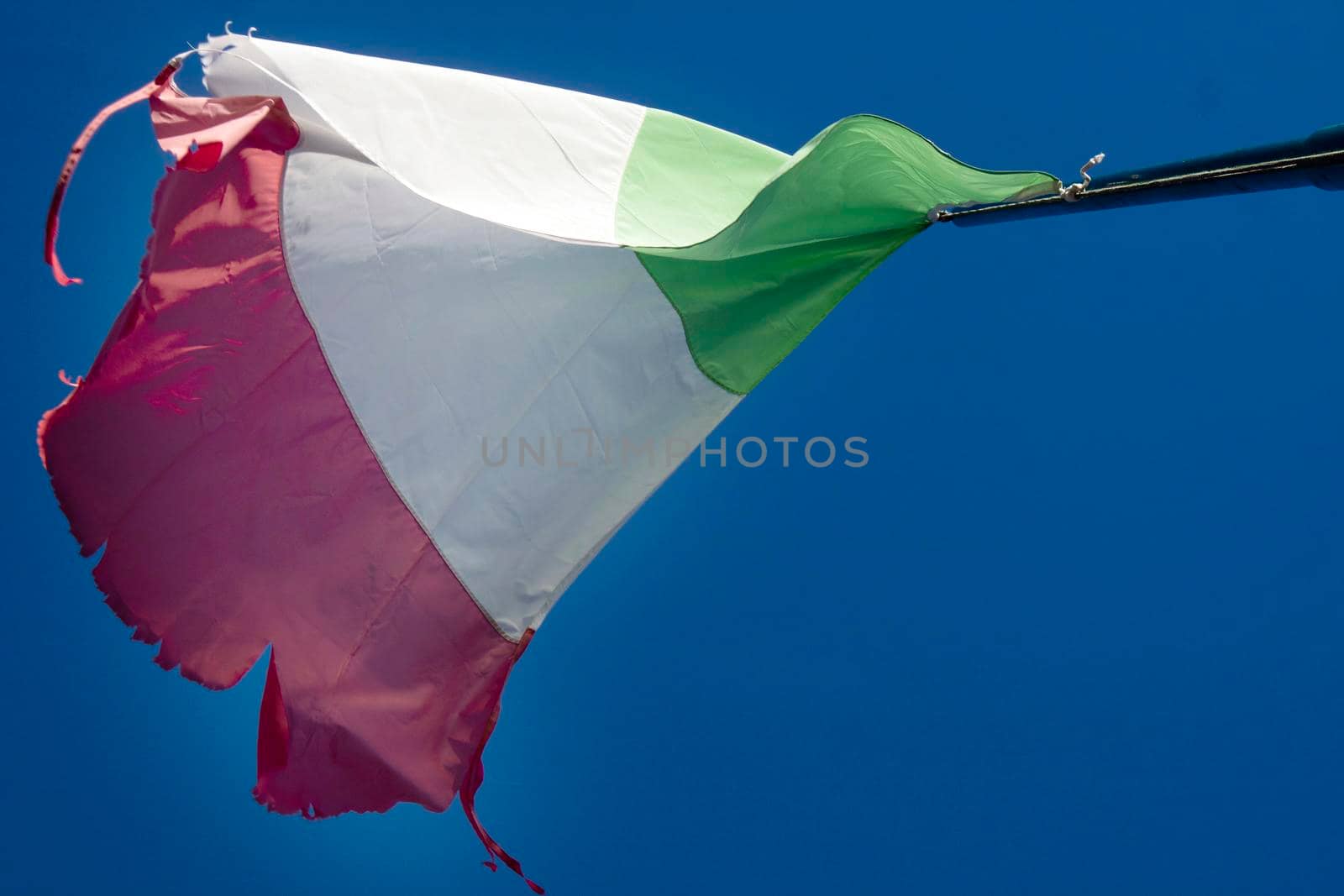 The Italian tricolor flag worn and torn by the wind in a blue sky 