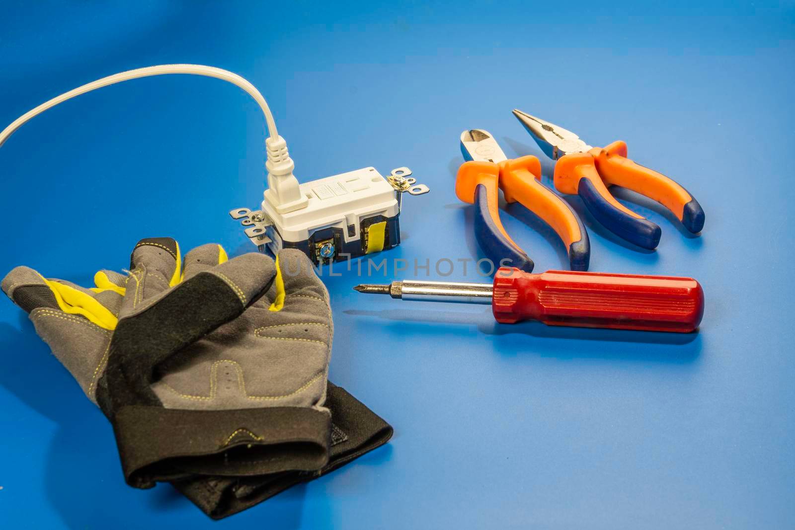 Gloves, electric socket with electrician's tools lie against a blue background