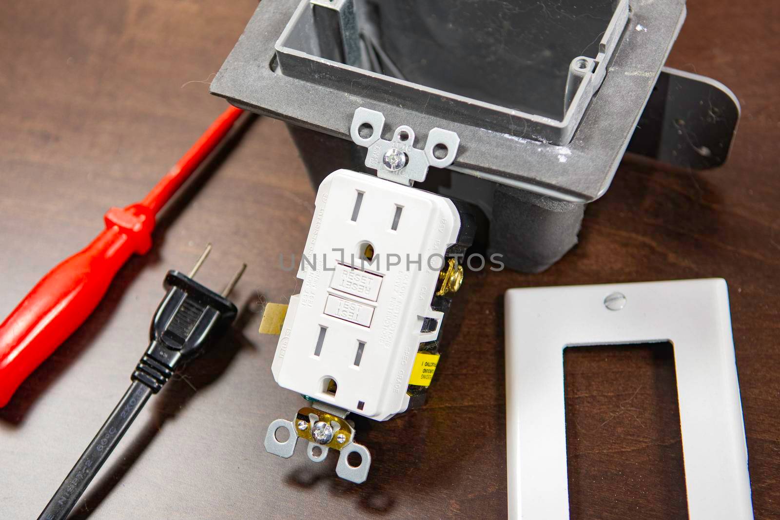 A tested electrical outlet lies on the table before being installed in a junction box on the wall.