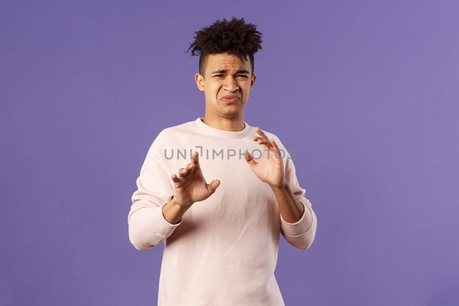 Phew get it away from me. Portrait of disgusted young man smelling something awful, step away and blocking it with raised arms, refuse grimacing with aversion and reluctance, purple background.