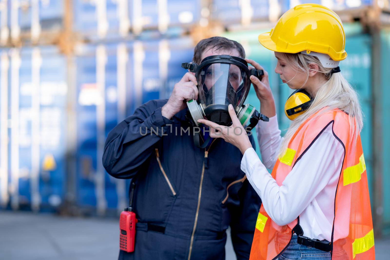 Cargo container woman worker help technician to wear gas protective mask and prepare for manage the problem in workplace area. by nrradmin