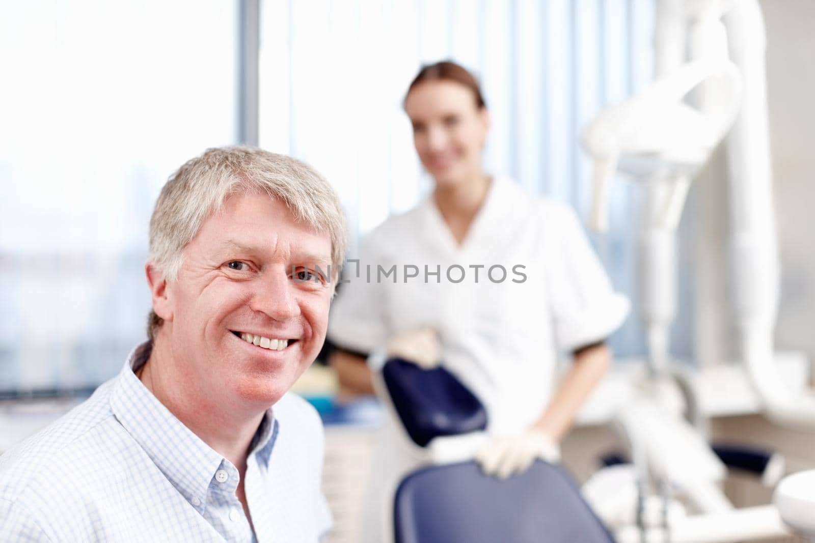 Smiling doctor with assistant. Portrait of handsome dentist smiling with his assistant in office. by YuriArcurs
