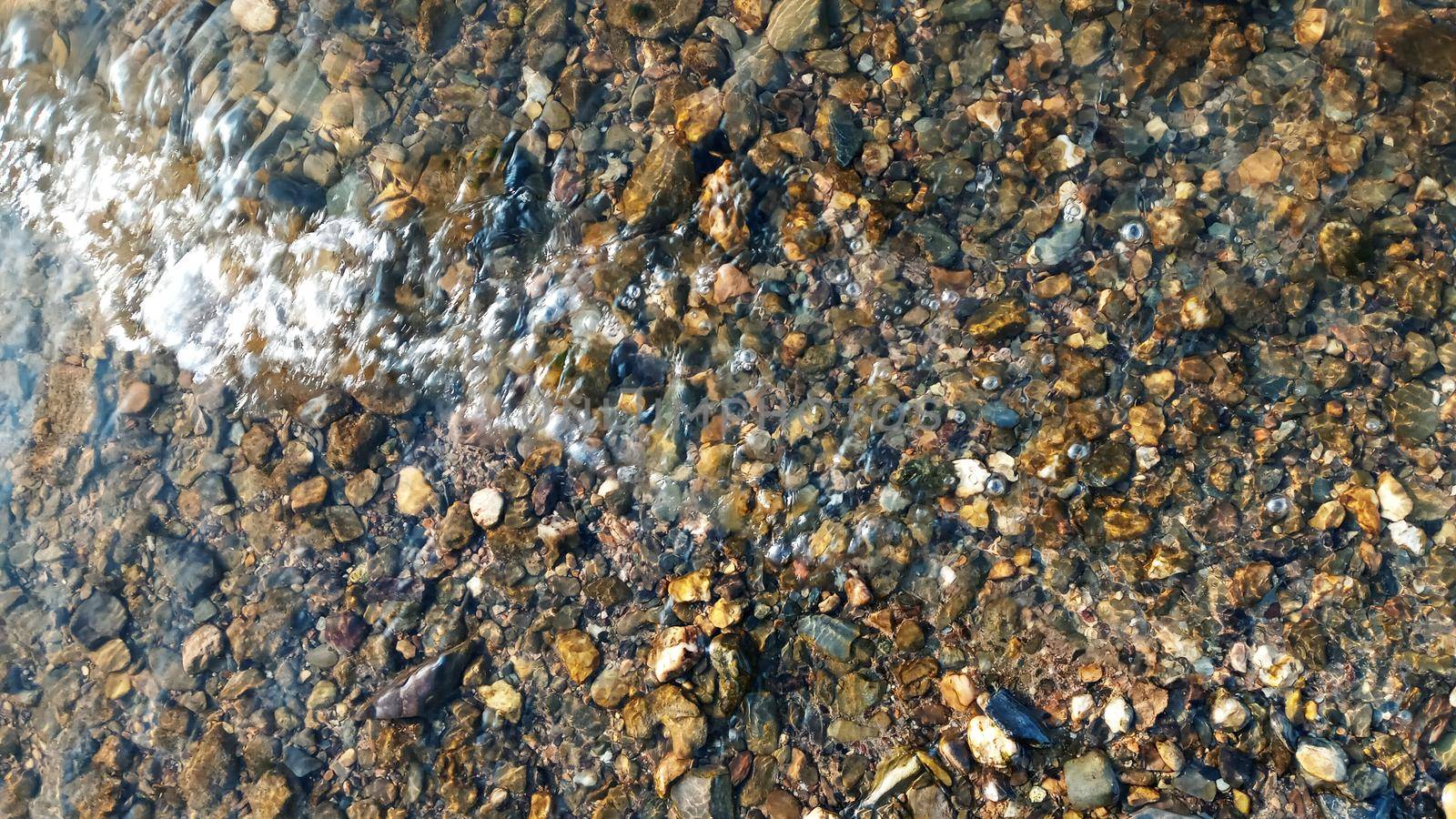 Top view on colorful pebbles covered by water. Close up view of smooth round pebble stones on the beach.