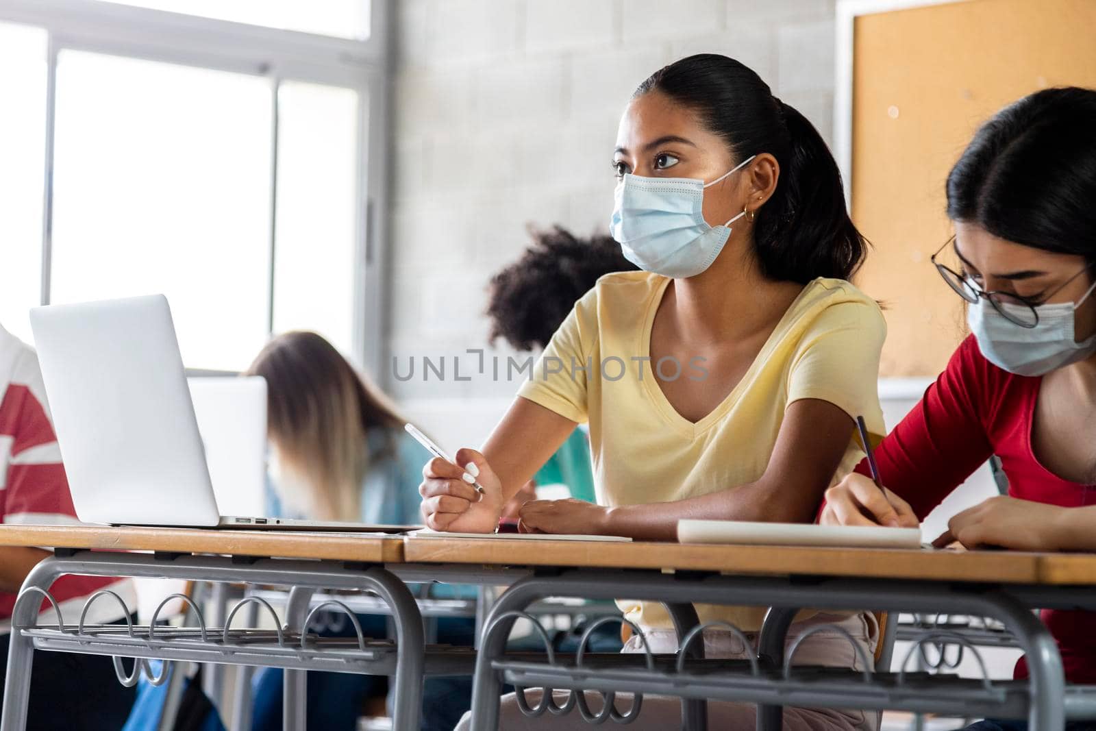 Teen latina girl student wears protective face mask in high school class. Copy space. by Hoverstock