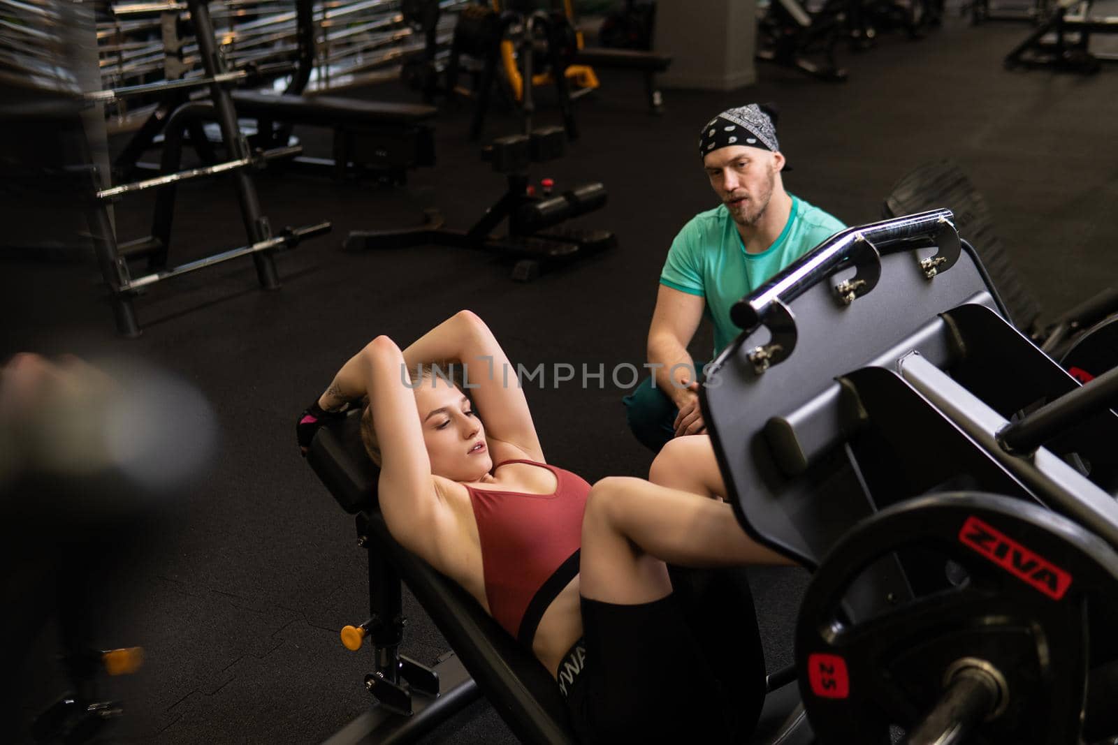 RUSSIA, MOSCOW - FEB 11, 2022: A girl is engaged in a led press simulator in a red blonde beautiful on a black background leg gym training press muscles, for healthy workout for fit from caucasian athletic, power length. Shape working beautiful, adult trainer by 89167702191