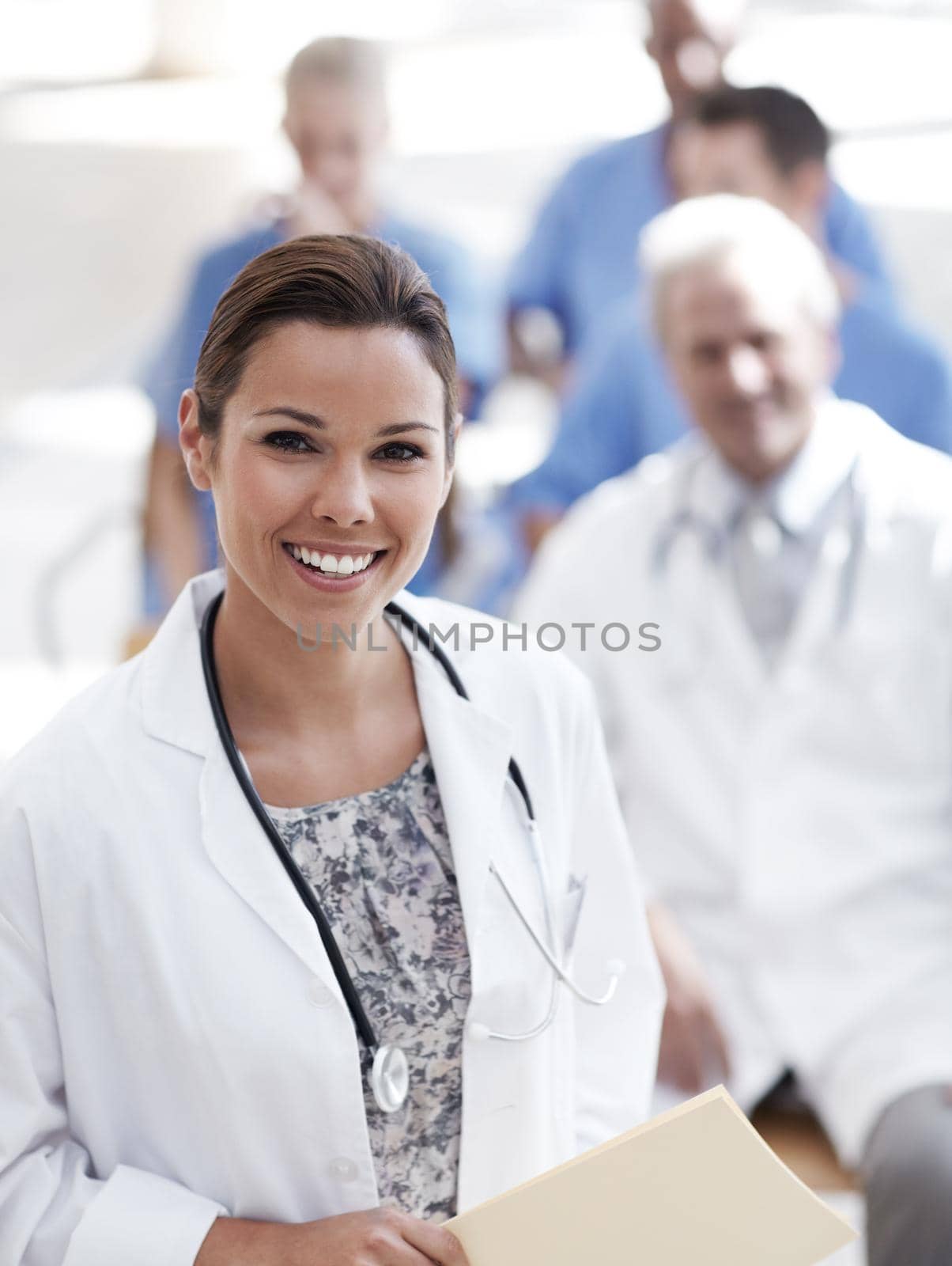 Looking after all your medical needs. A doctor standing with colleagues sitting in the background. by YuriArcurs