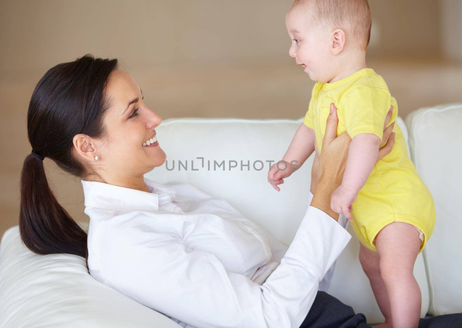 Beautiful young mother playing with her baby on her couch.