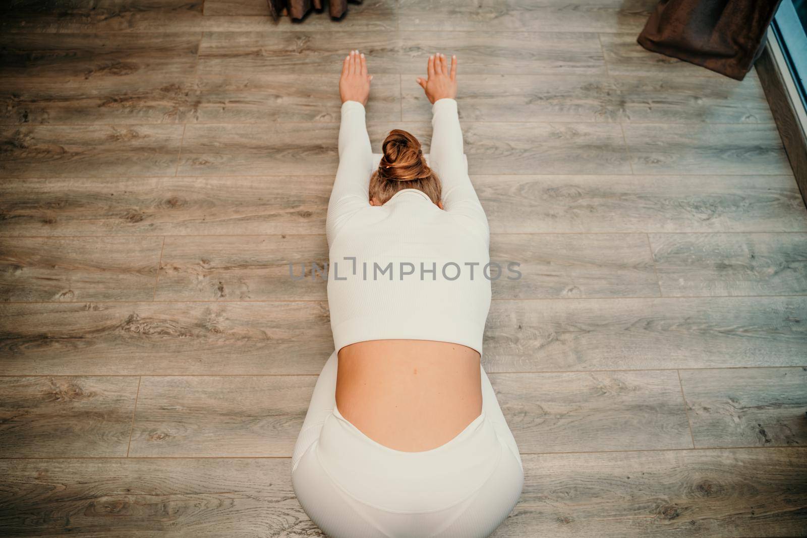 Adult athletic woman, in white bodysuit, performing fascia exercises on the floor - caucasian woman using a massage foam roller - a tool to relieve tension in the back and relieve muscle pain - the concept of physiotherapy and stretching training.