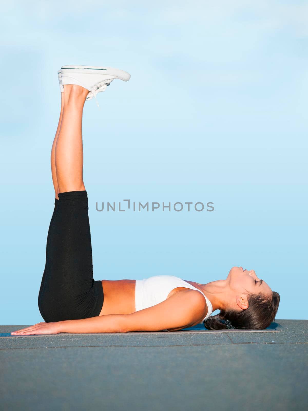 A young woman doing yoga outdoors against a blue sky.