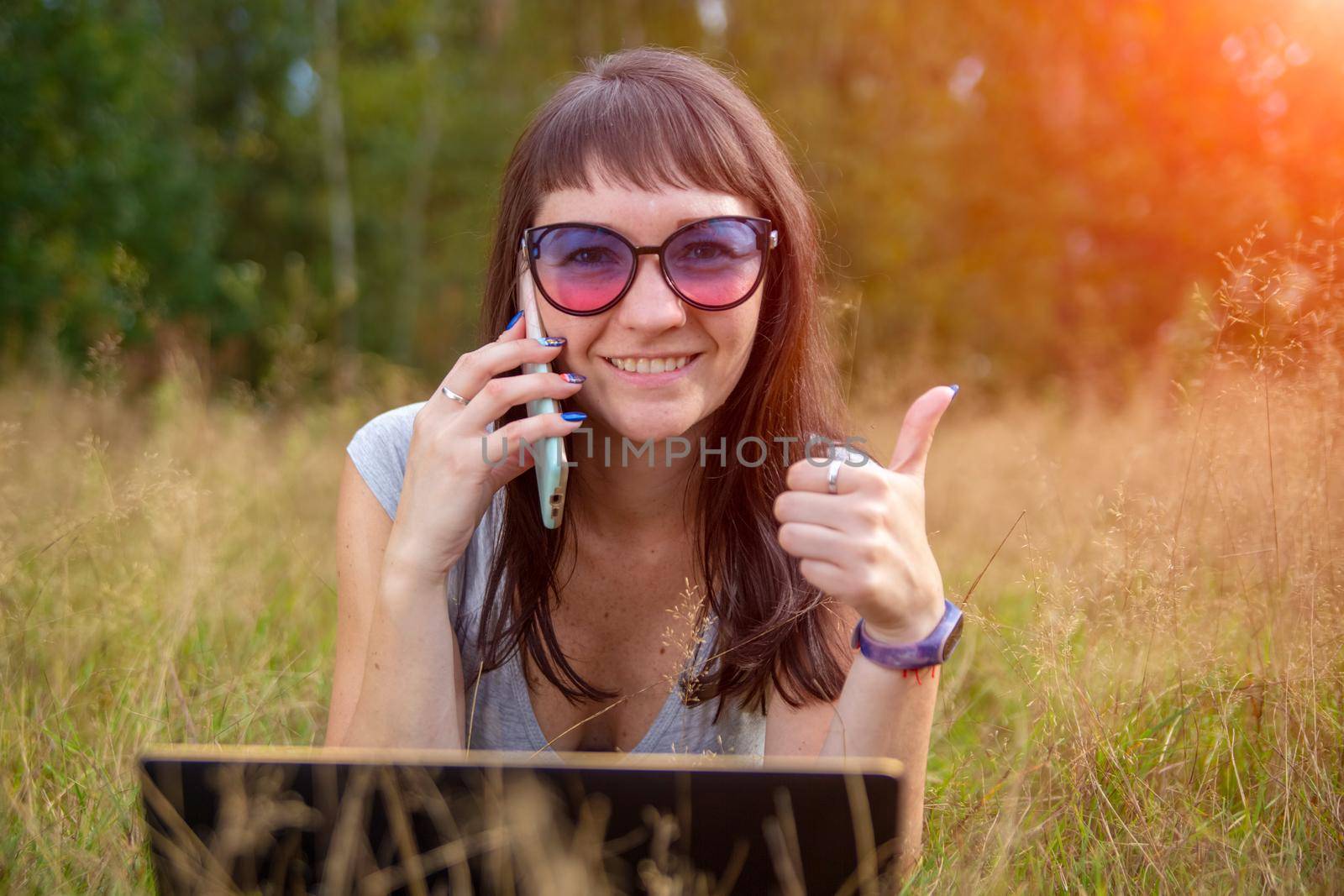 young woman calling by phone and smiling happy on summer lawn outdoors by Mariaprovector