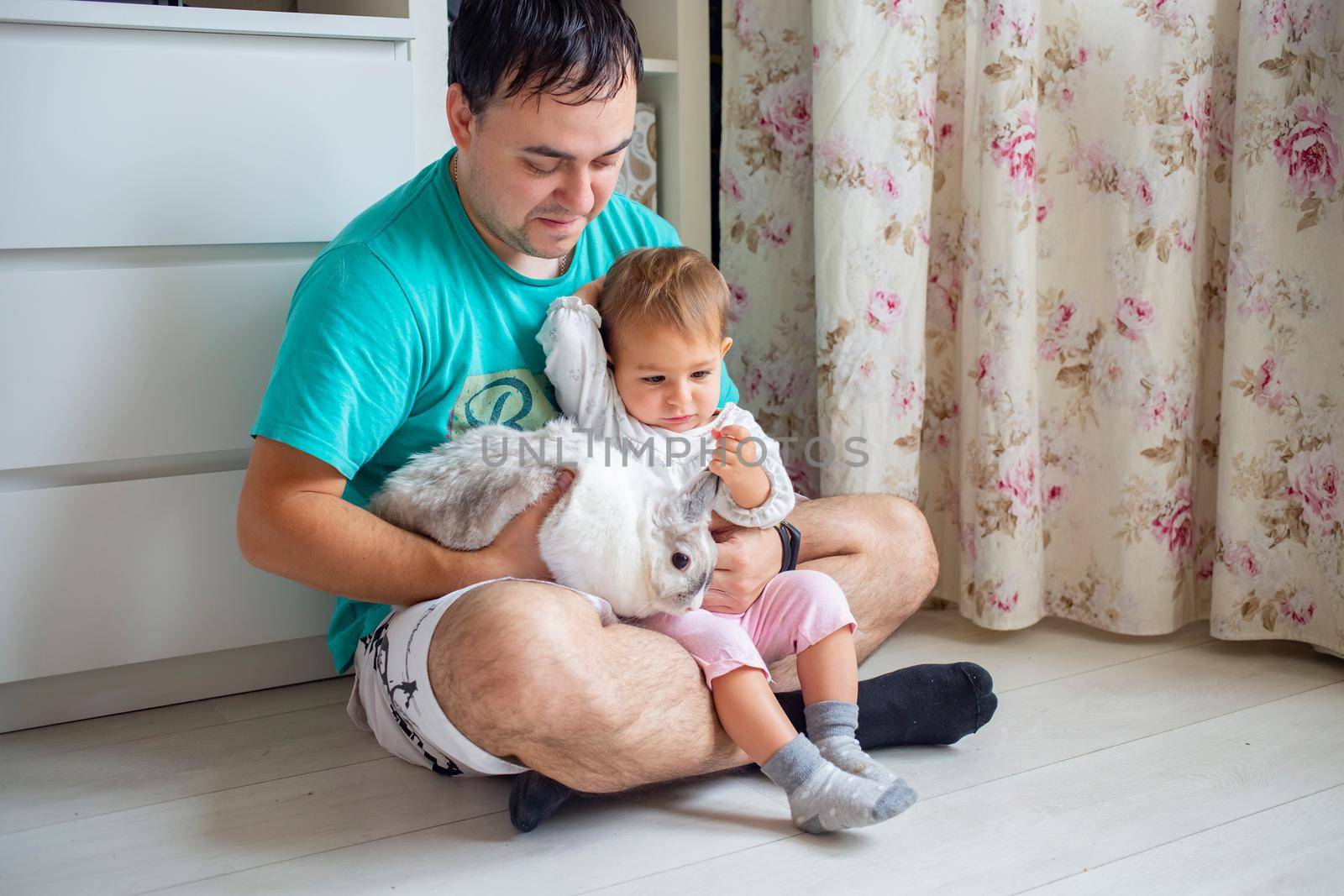 cute little baby play with decorative rabbit in fathers arms at home. domestic animals and children by Mariaprovector