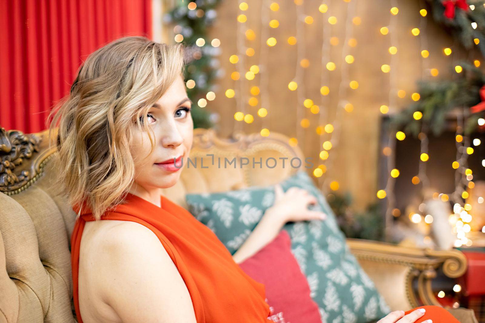 beautiful blonde young woman sitting in a room decorated for the new year celebration by Mariaprovector