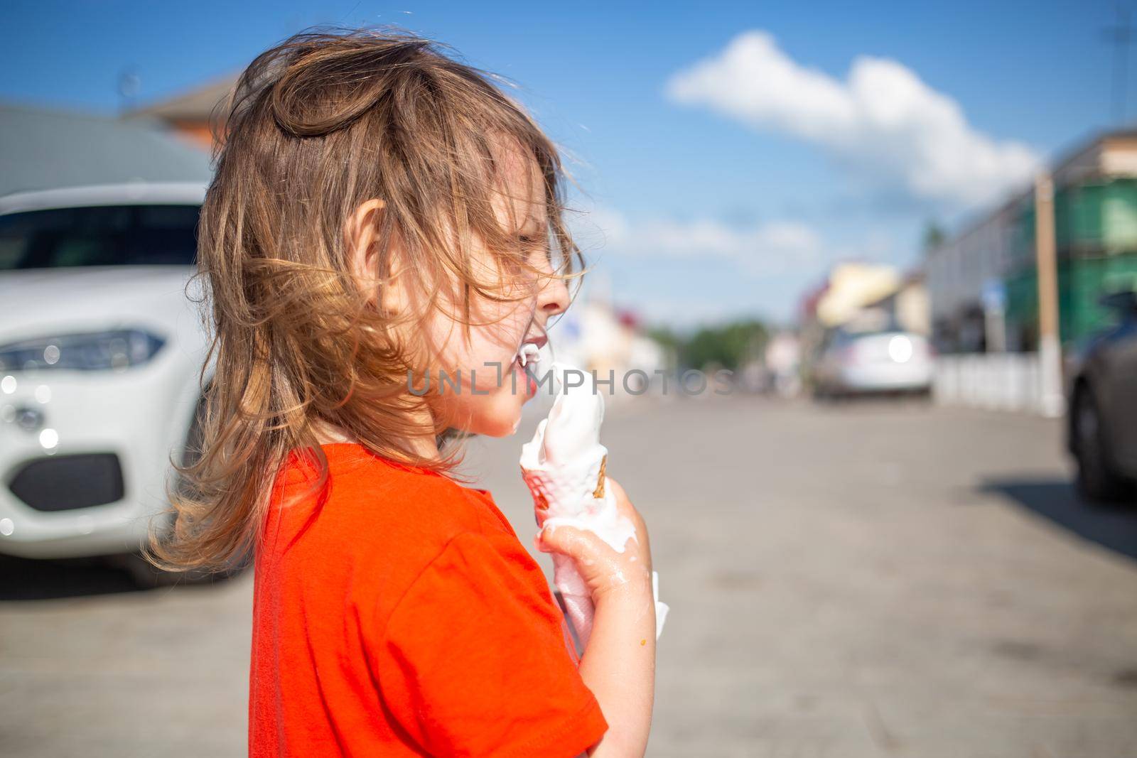 side portrait of little girl eating an ice cream cone on a hot day outside. ice cream melts and flows