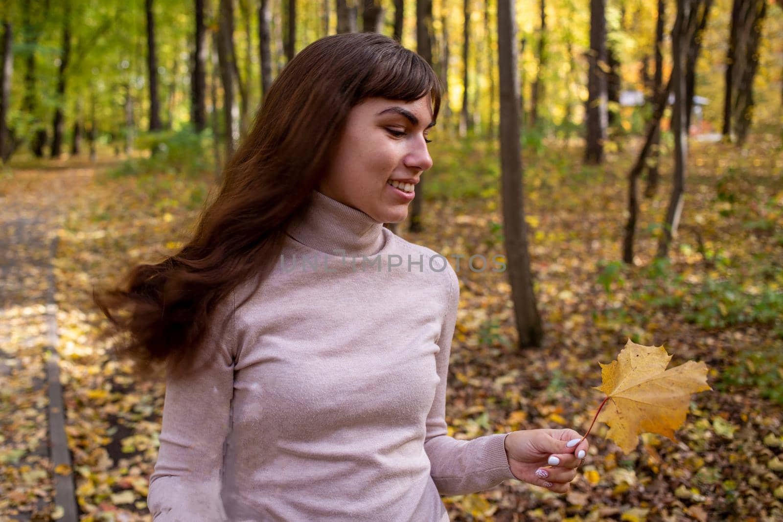young beautiful woman with autumn leaf smiling in autumn park in sun shines.happy young woman by Mariaprovector