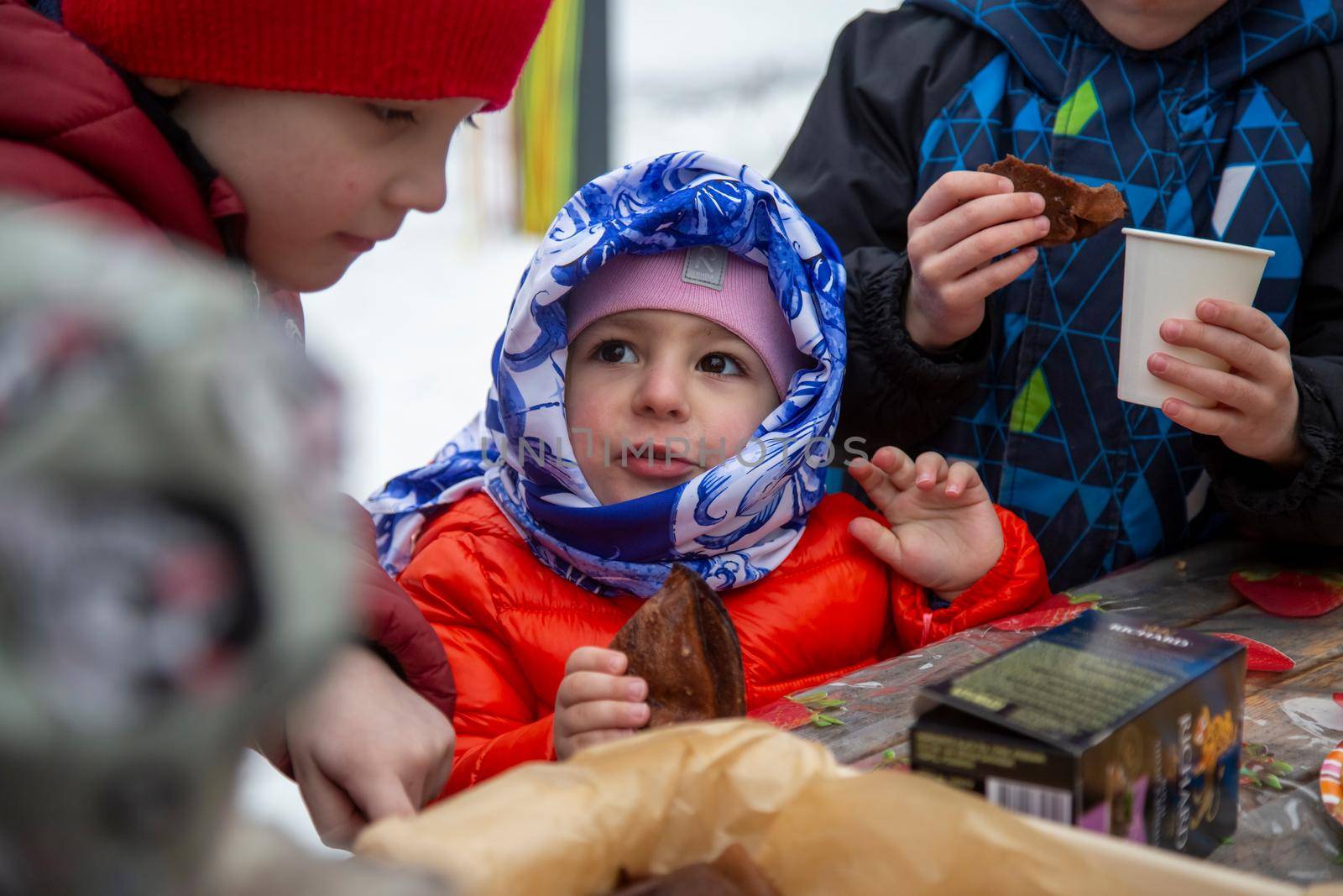 little girl eating pancake blini at maslenitsa festival by Mariaprovector