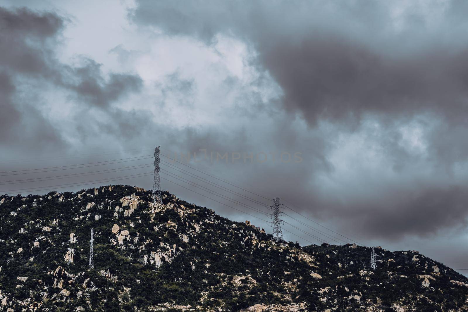Real nature landscape background. Rocky mountain, cloudy Pale Blue dark stormy sky autumn day, high voltage Electricity power pylons. Cold mood feelings. Problem Difficult obstacles, discomfort.