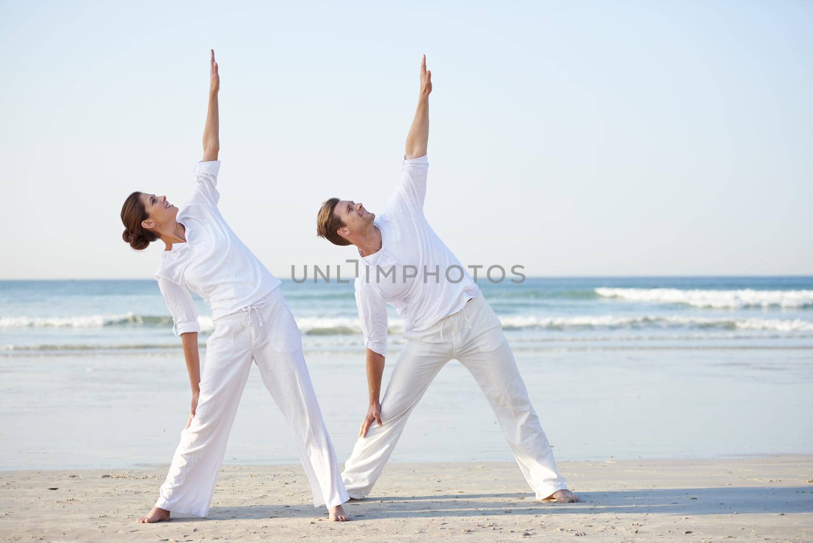A young couple practising yoga on the beach.