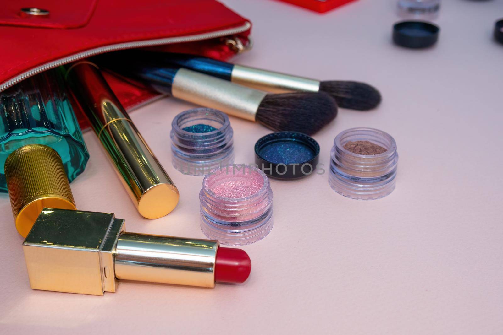 Top view of cosmetics standing out from beige makeup bag on pink background. Photo