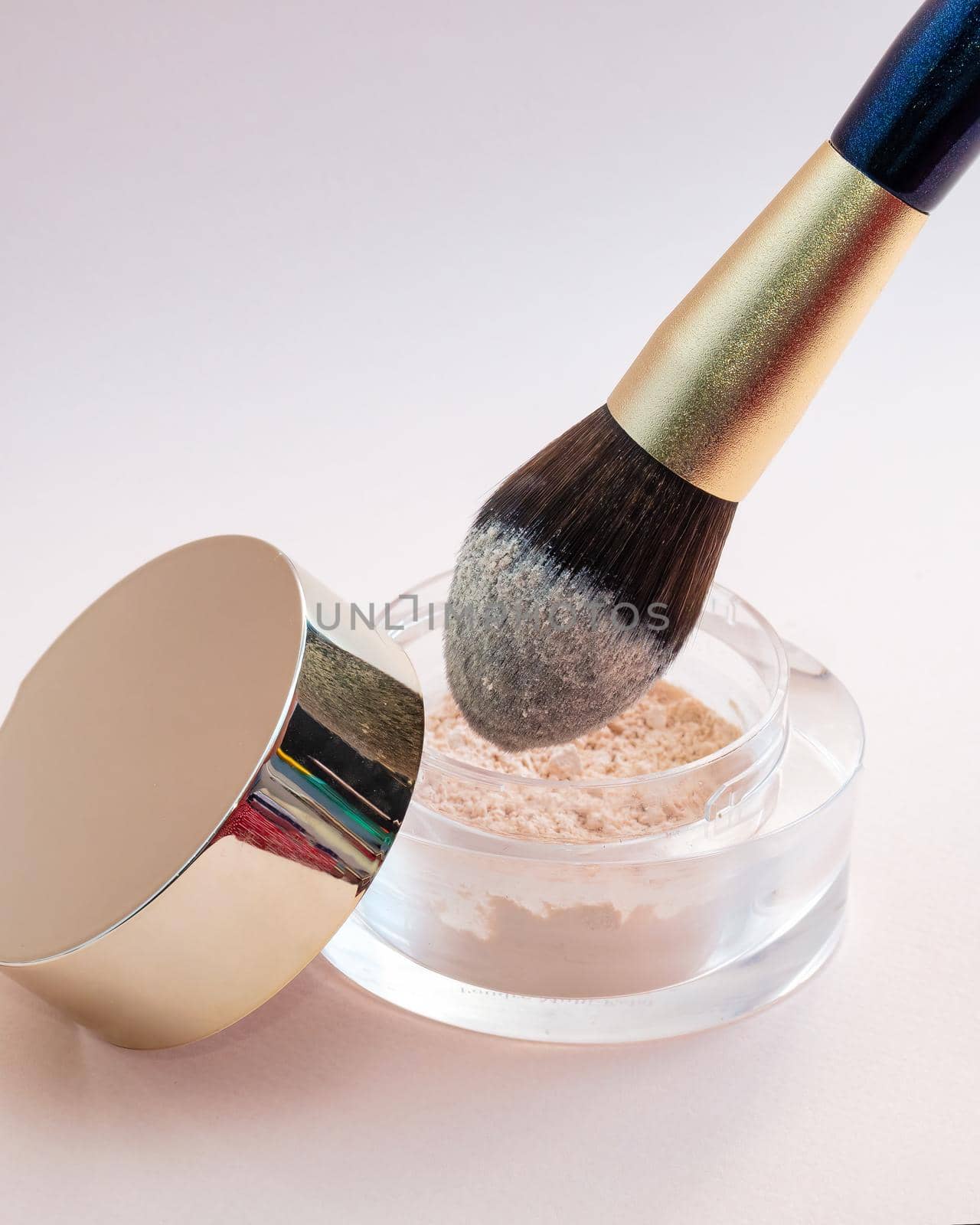 A golden makeup brush is dipped in a glass jar with powder on a pink background. by Andre1ns