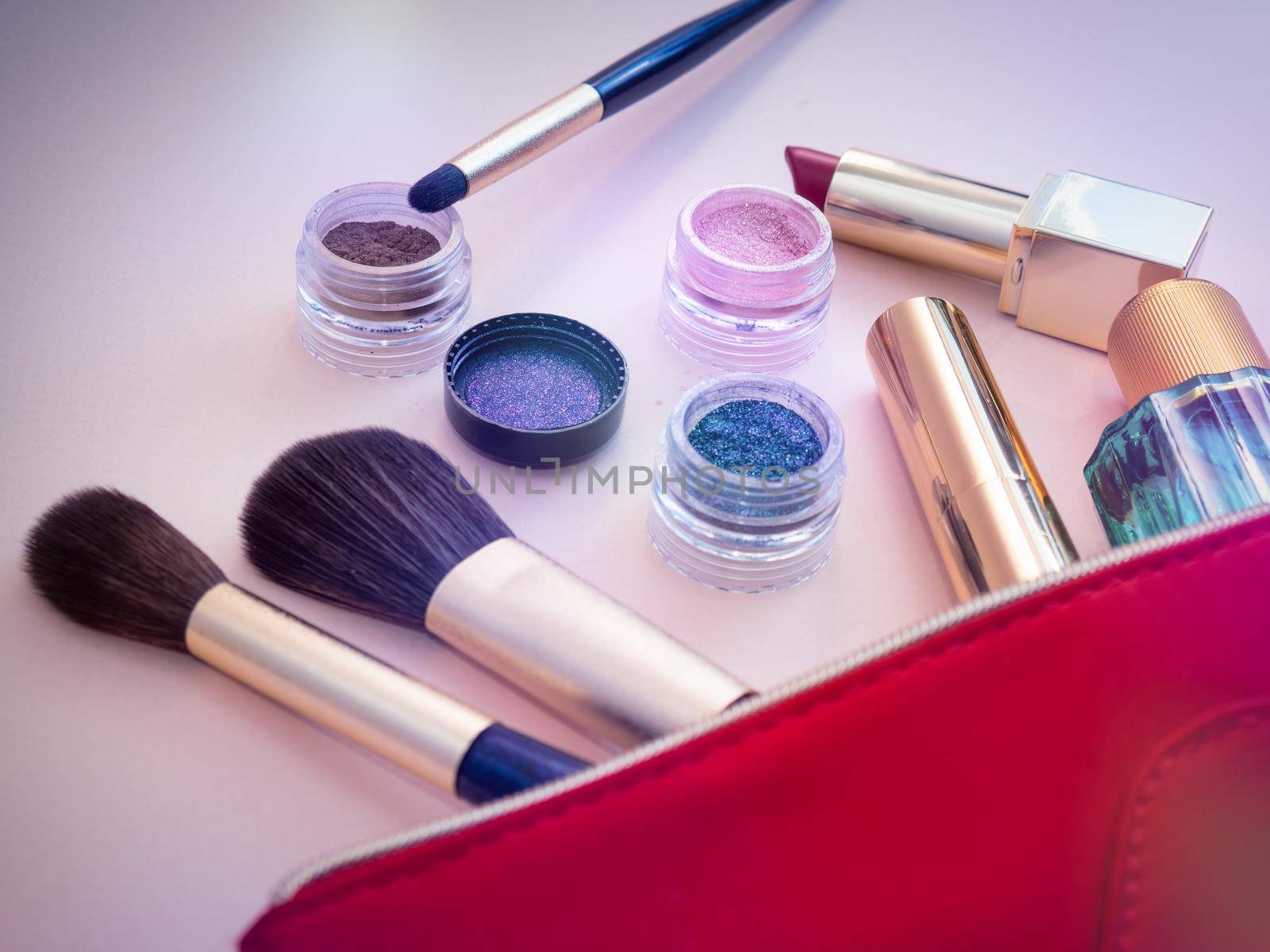 Top view of cosmetics standing out from red cosmetic bag on pink background by Andre1ns