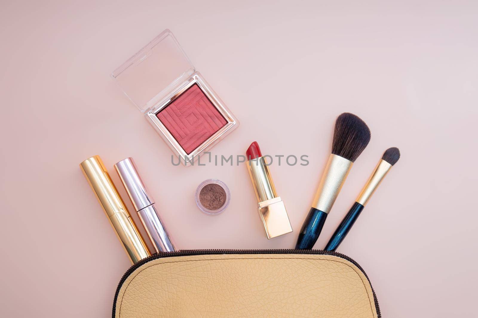 Top view of cosmetics standing out from beige makeup bag on pink background. Photo